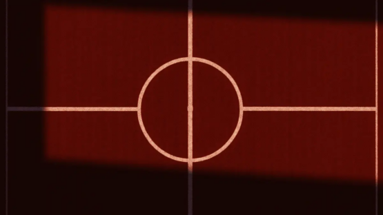 Overhead view of a floodlit football pitch with red grass and white markings at sunset.