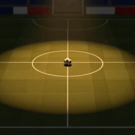 Empty floodlit football pitch at dusk with centre spot ball and flag-coloured stand accents, aerial view.