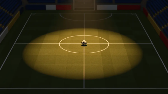Empty floodlit football pitch at dusk with centre spot ball and flag-coloured stand accents, aerial view.