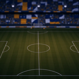 Aerial view of floodlit stadium pitch with geometric markings and flag-coloured stand sections at dusk, group-stage atmosphere.